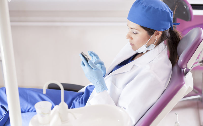Joven dentista opera su smartphone usando guantes