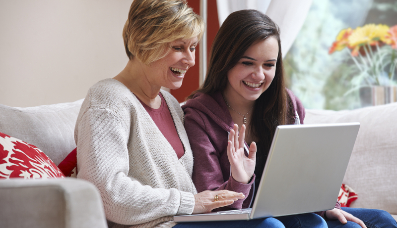 Dos mujeres, una adulta y una adolescente, miran sonrientes la pantalla de un laptop.