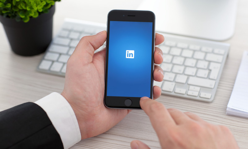 Ejecutivo sostiene smartphone en cuya pantalla se ve el logotipo de LinkedIn