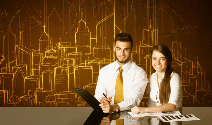 Pareja de ingenieros o ejecutivos sentados frente a mesa negra, con edificios y números como imagen de fondo